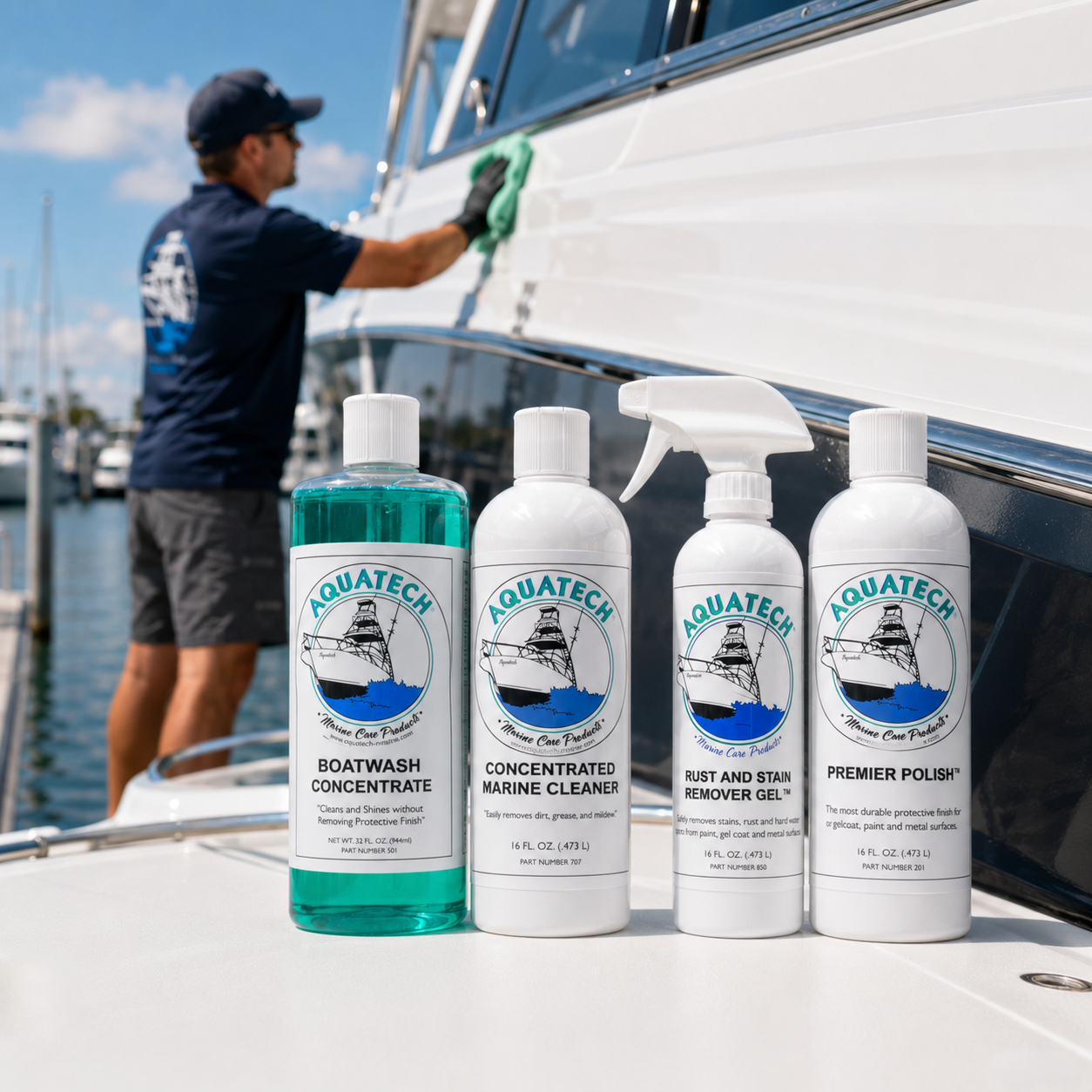 Four Aquatech marine cleaning products displayed on a white boat deck in front of a marina scene, with a man washing a boat in the background.